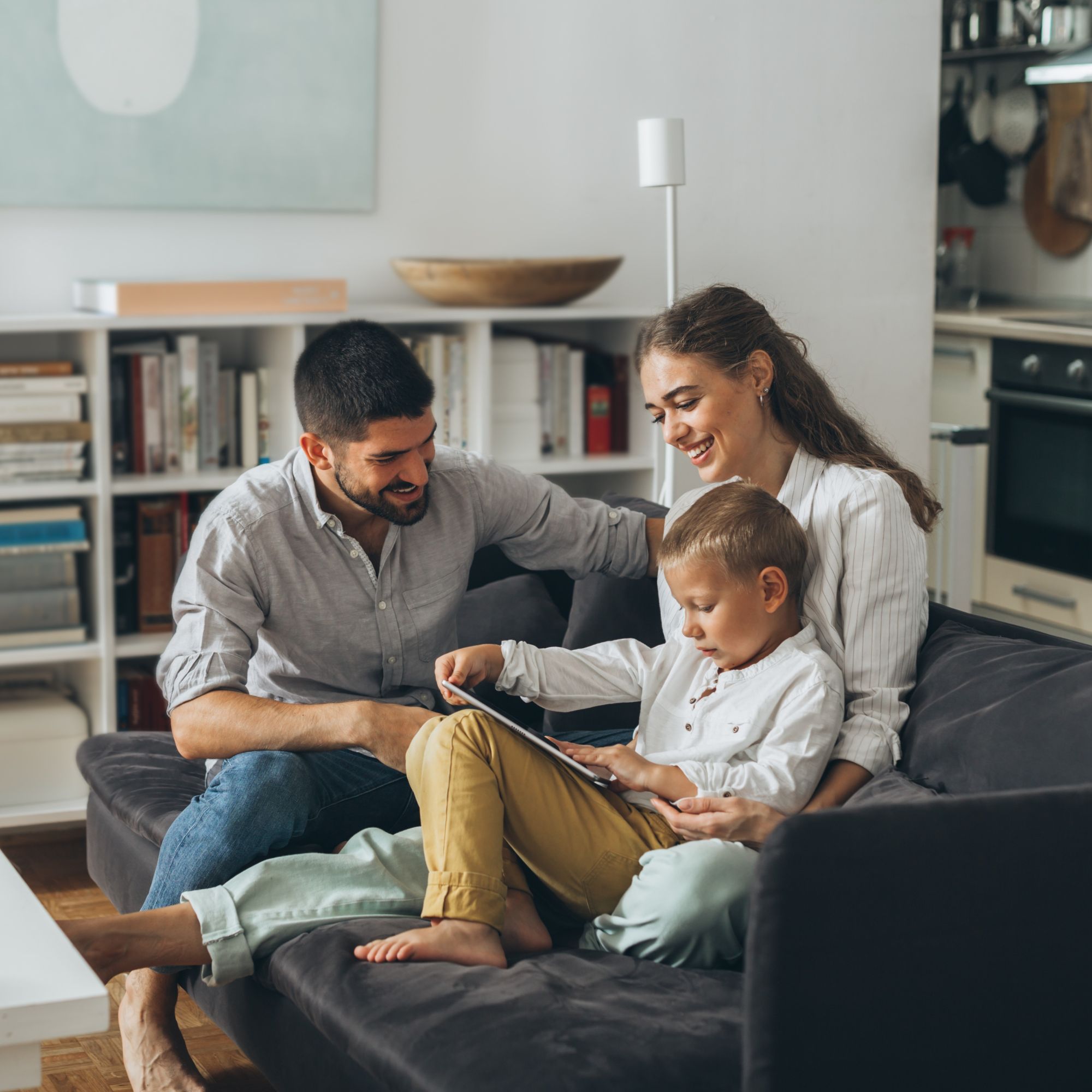 Father, mother and their child sitting on their living room couch and smiling, comfortable in their home
