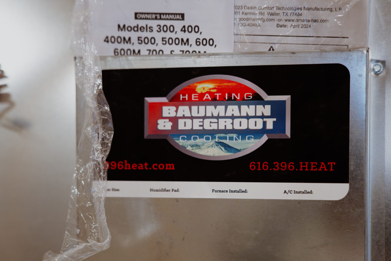 Baumann & DeGroot logo featured on furnace sheet metal, along with hvac system maintenance history. Contact information such phone number and website is located above humidifier pad, furnace installation, and AC installation. 